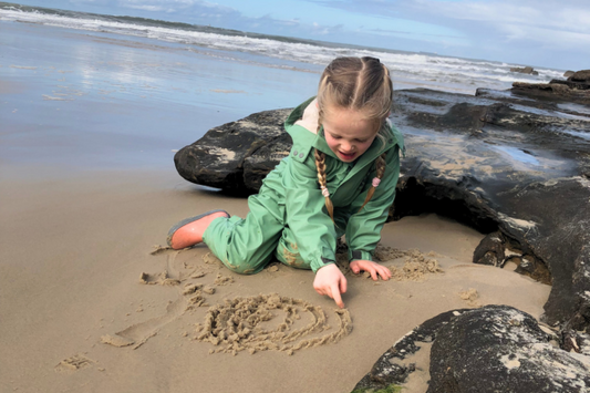 Young toddler kid drawing in the sand at the beach in winter, wearing her kids waterproof suit