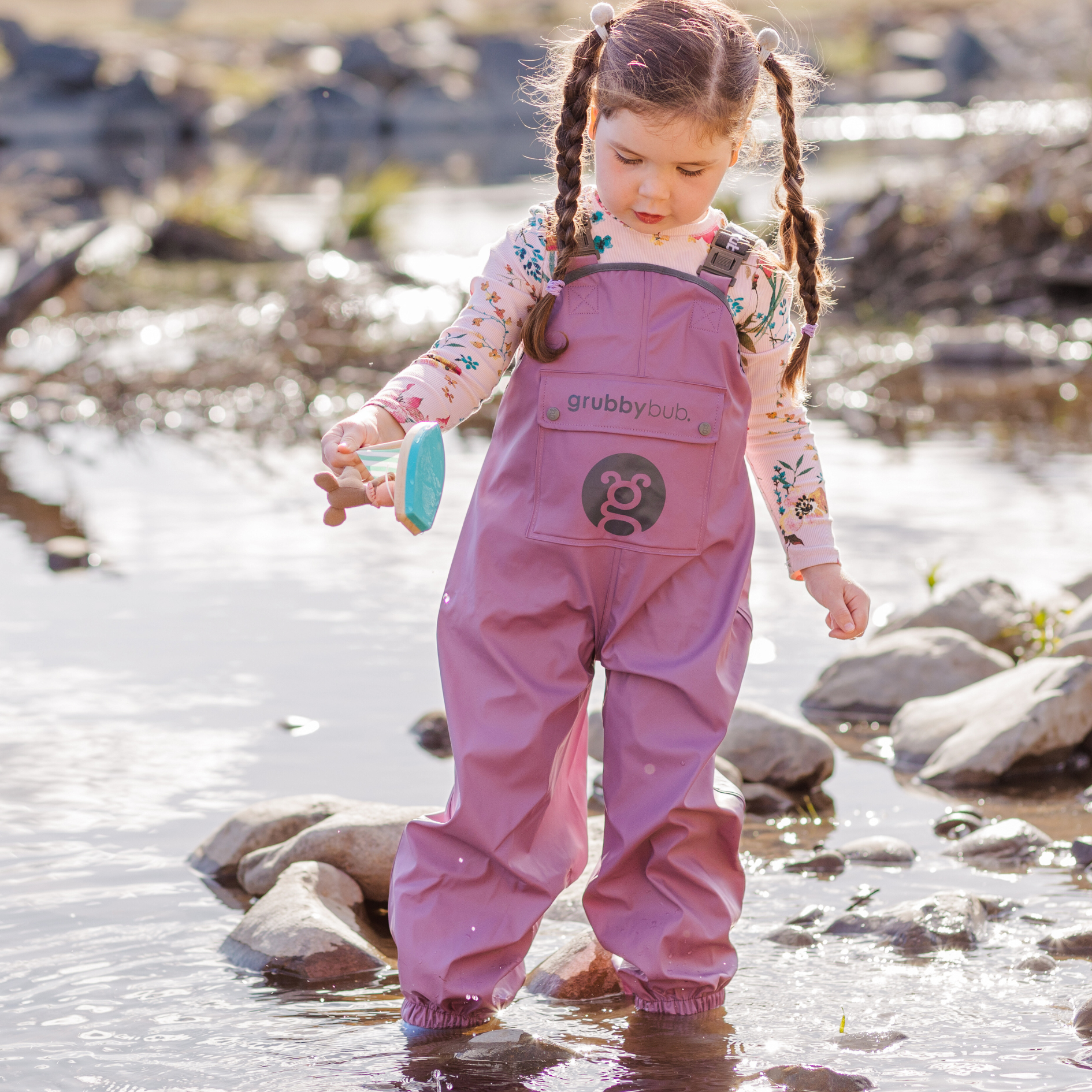 Toddler in waterproof bib overalls playing in water, kids outdoor clothing for messy play and exploration