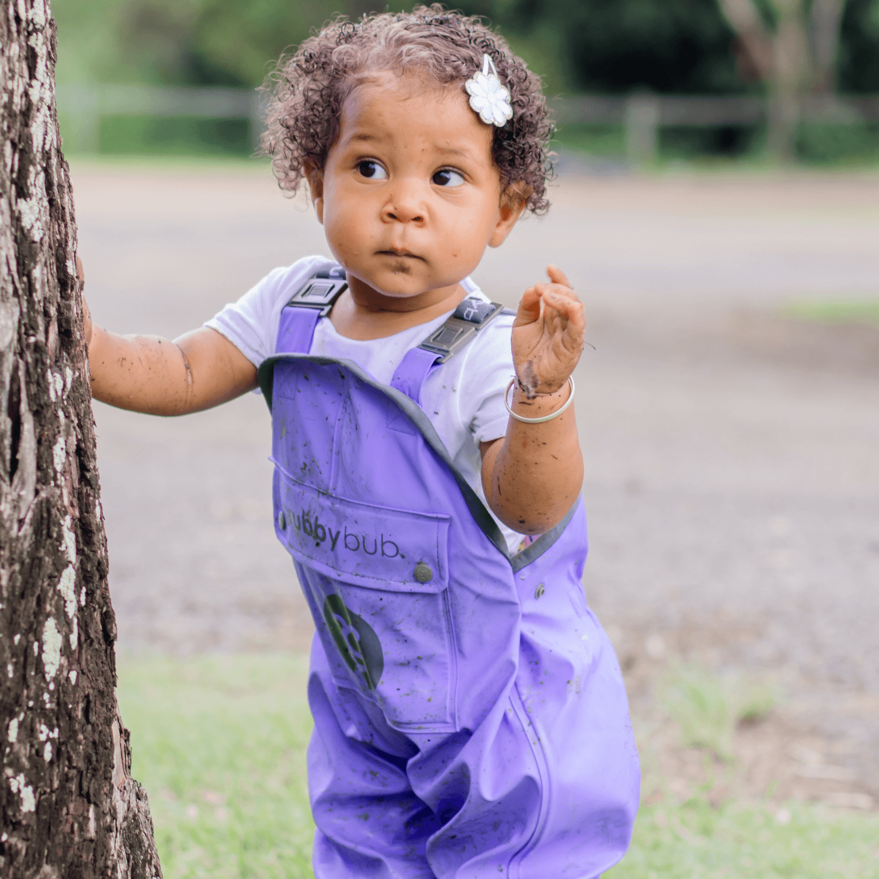Child in waterproof overalls exploring tree with muddy hands during sensory play